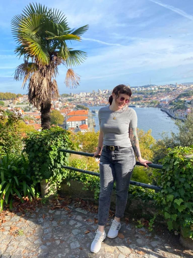 woman smiling surrounded by greenery with a view of Porto, Portugal in the background