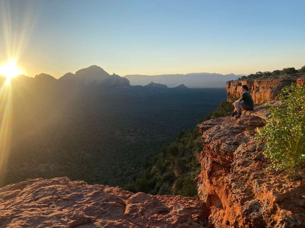 woman sitting on rocky outcrop watching the best sunrise view from Doe Mountain in Sedona Arizona