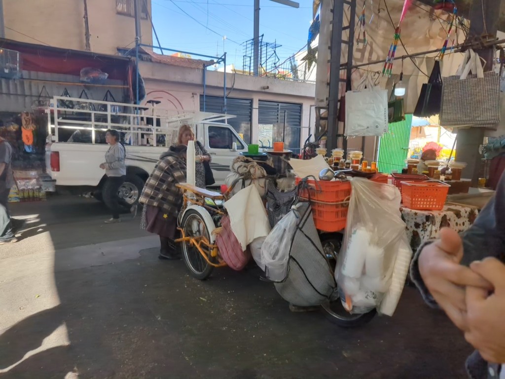 a woman kneeling over a bike and cart covered in various bags and pots serving tamal sandwiches and atole in CDMX street food tour