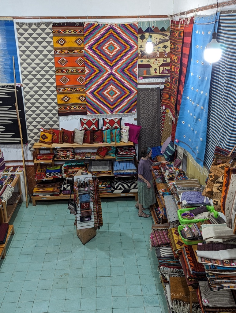 a woman looking a woven rugs and other goods in a textile shop in Oaxaca Mexico