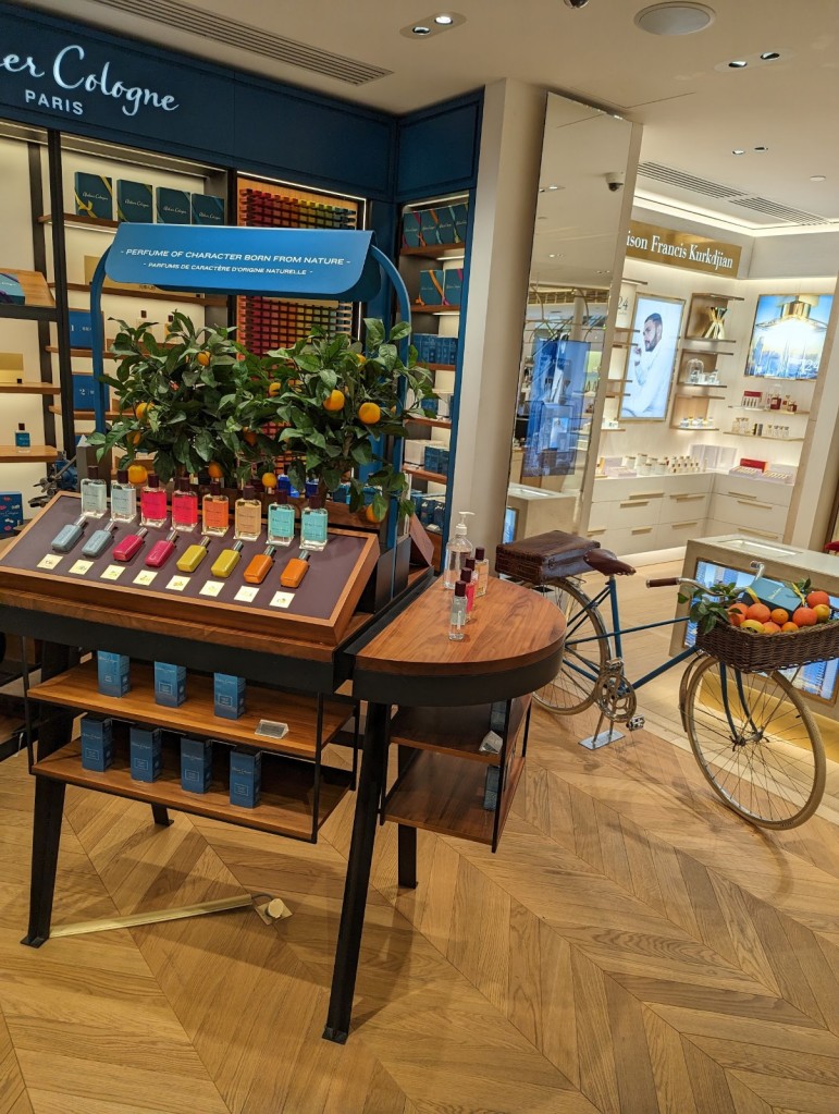 Atelier cologne perfume display in a French department store with colorful bottles and a bike with a basket full of oranges